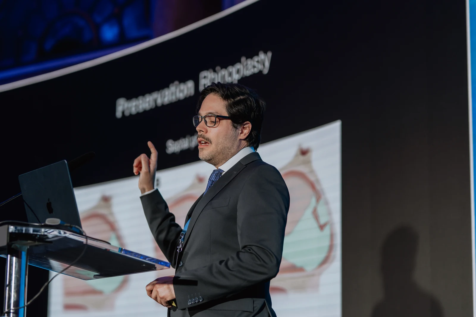 El Dr. Gustavo Suárez explica una técnica durante una conferencia, con la mano levantada